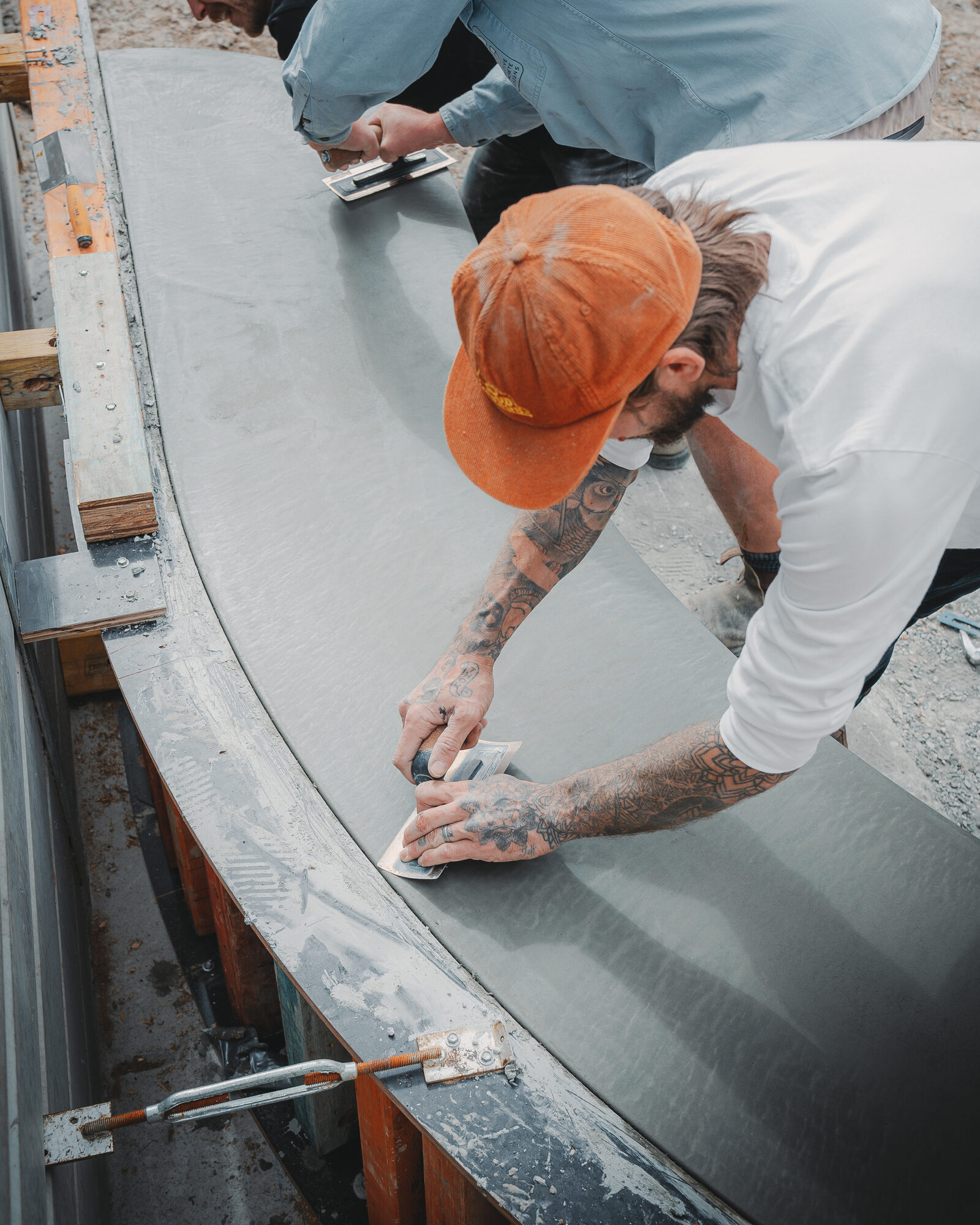 Two artisans hand-troweling a curved wet concrete form