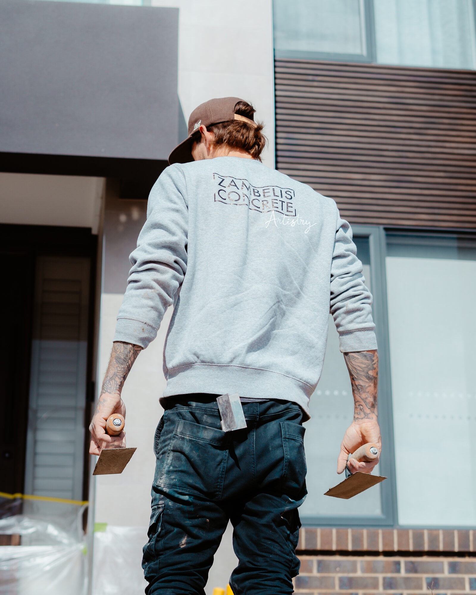 Branded artisan from behind holding concrete finishing trowels