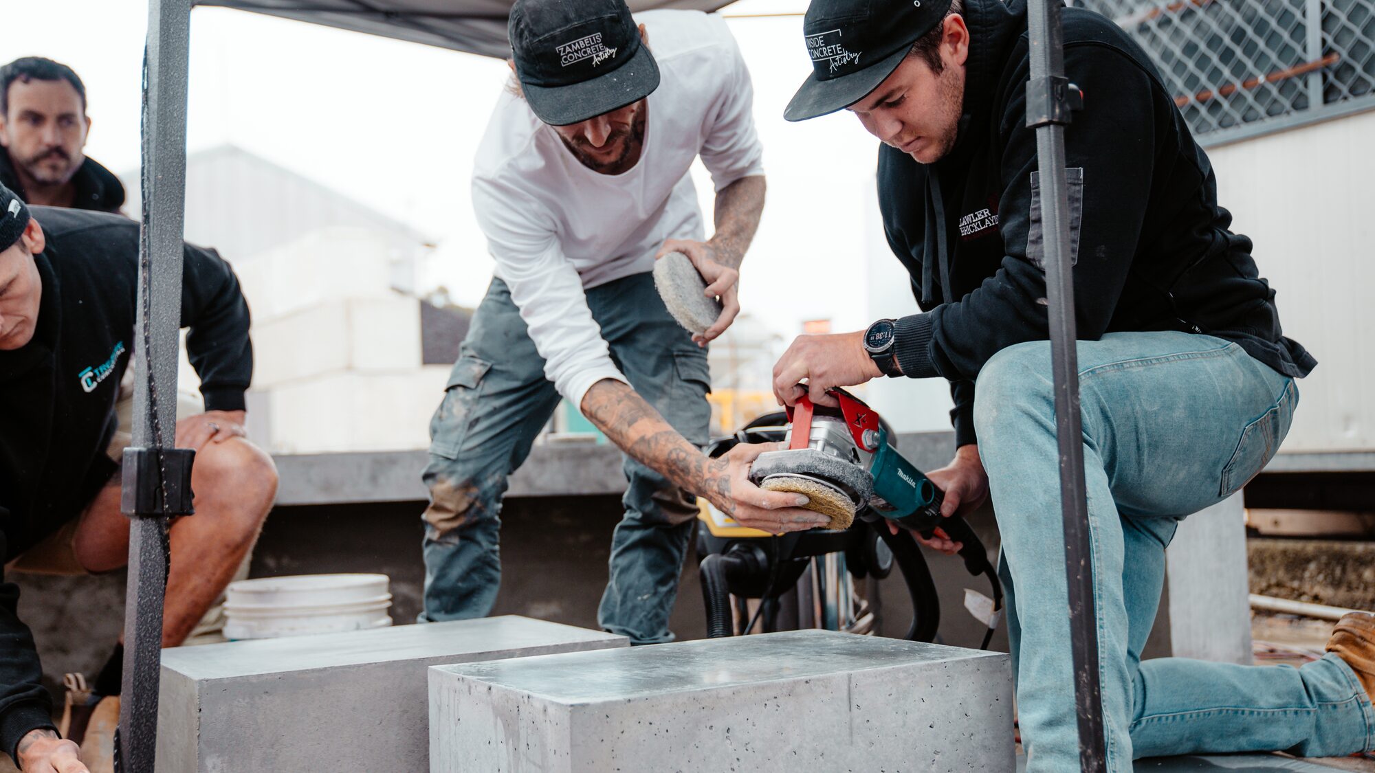 Trainees polishing concrete blocks under a pop-up shelter